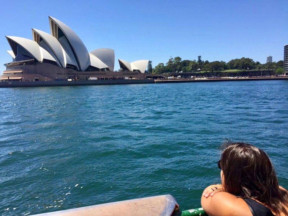 Vivir Sydney chica de espaldas contemplando la Ópera de Sydney y el cielo despejado